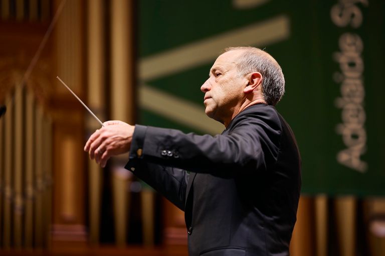 Conductor Mark Wigglesworth holding a baton in mid-performance on stage with the Adelaide Symphony Orchestra. Photo by Claudio Raschella.